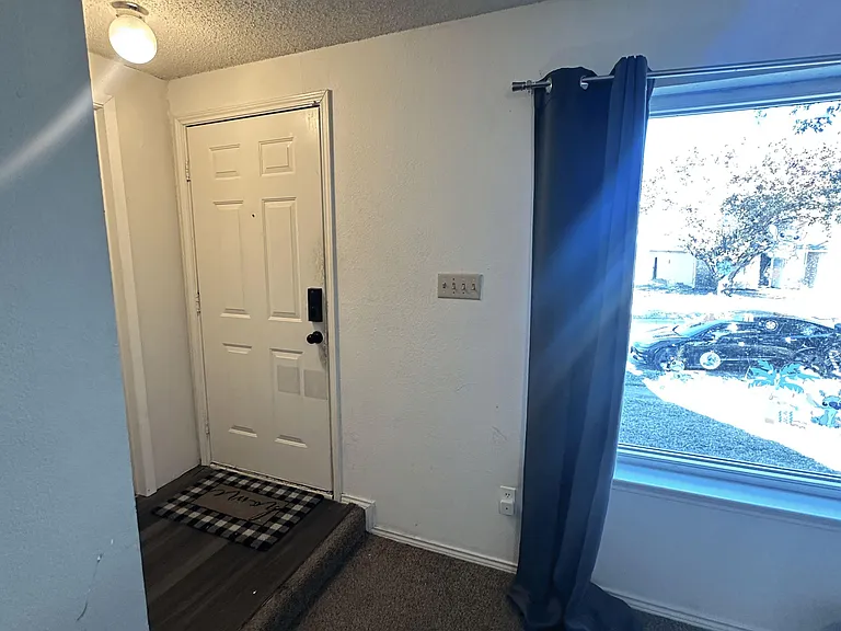 Entry foyer with a front door landing, carpeted flooring, and a large window with curtain panels for natural light.