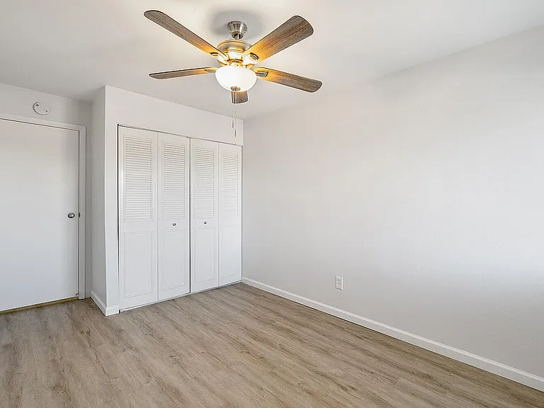 Bright and airy room with modern fan, sleek wooden flooring, and ample storage with white closet doors.
