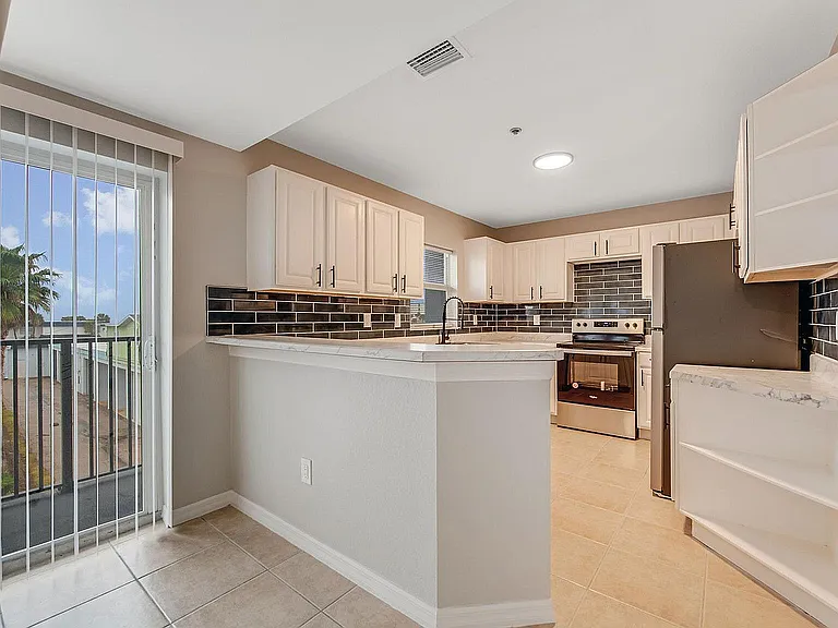 Contemporary kitchen with sleek black tile backsplash, marble countertops, and ample natural light through large windows.