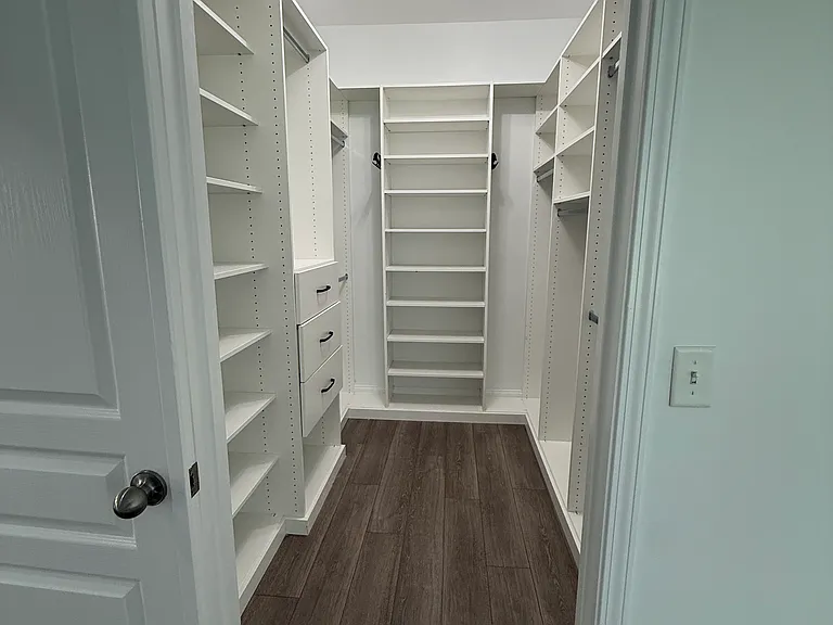 Luxurious primary suite walk-in closet custom designed by Closets by Design! Enjoy ultimate organization with floor-to-ceiling built-in shelving, integrated dresser drawers, ample hanging rods, and modern wood-look flooring."