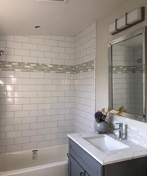 Beautiful bath with natural light. Tub/shower with white subway tile, glass/marble accents, gray maple shaker vanity, quartz counter, LED lighting, tile floors.