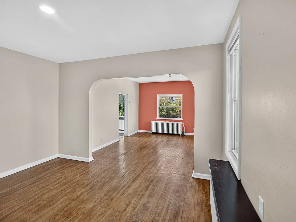 Open living and dining area highlighting original hardwood flooring and an elegant arched architectural transition.