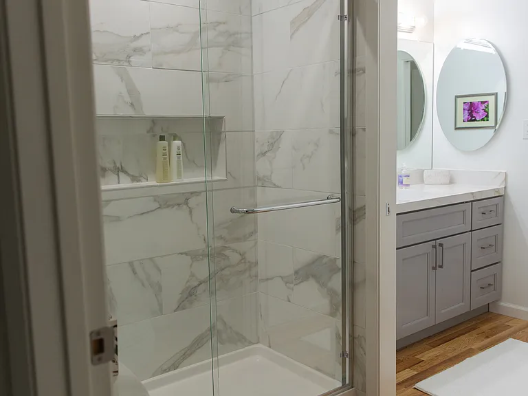 Newly renovated marble shower with barn doors and hardwood flooring. View towards 2nd vanity and sink.