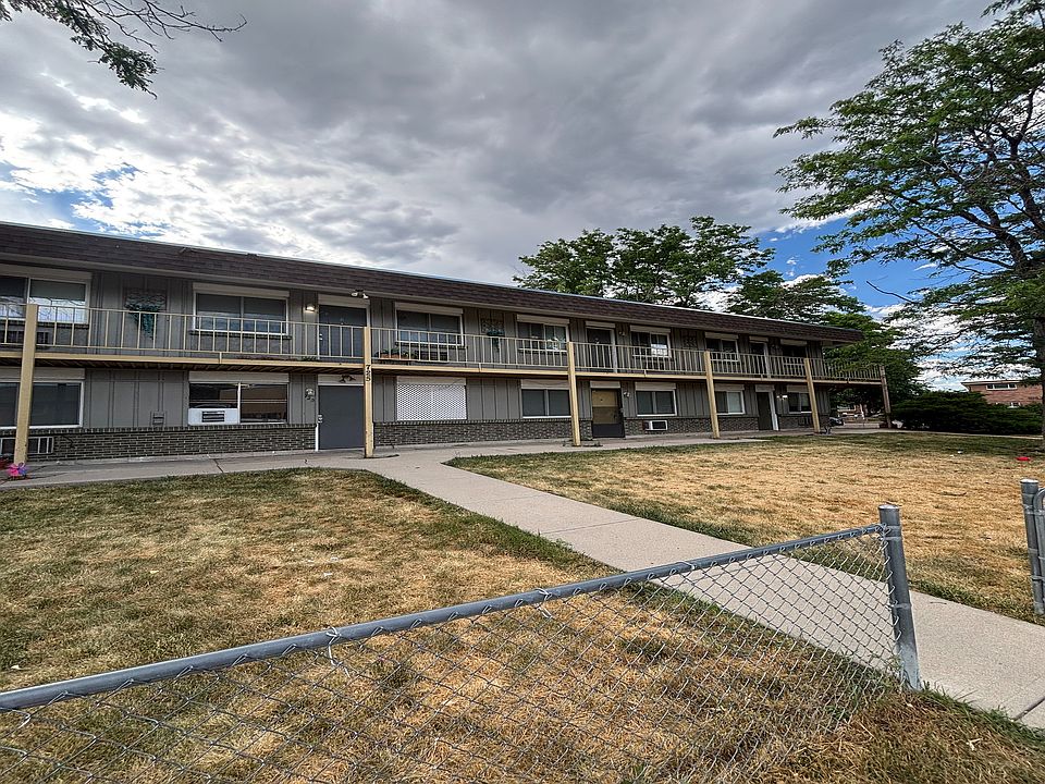 Charming two-story apartment complex with a spacious balcony, surrounded by lush greenery and a clear blue sky, offering a serene living environment.