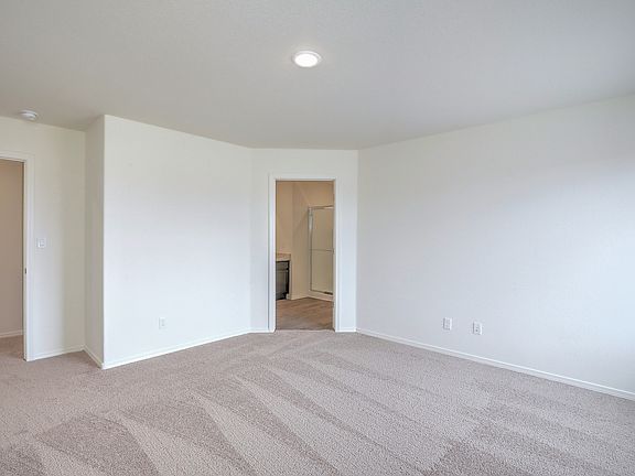 Master bedroom with tan carpet and a connected bathroom.