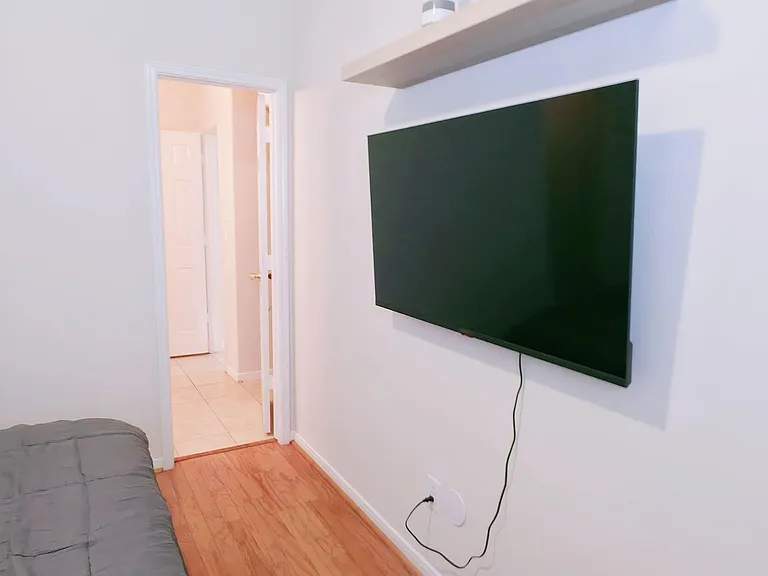 Private bedroom with hardwood floors, a wall-mounted TV, and convenient access to the hallway and nearby rooms.