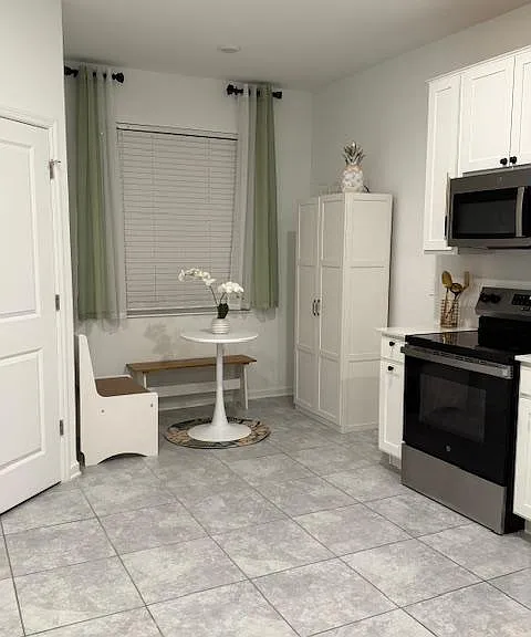 Eat-in kitchen area with white cabinetry, stainless range and microwave, and a small dining nook by the window.