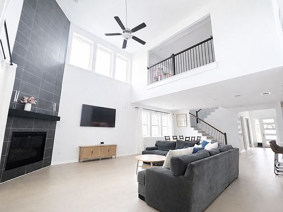 Spacious two-story living room with soaring ceilings, abundant natural light, and a dramatic floor-to-ceiling fireplace.