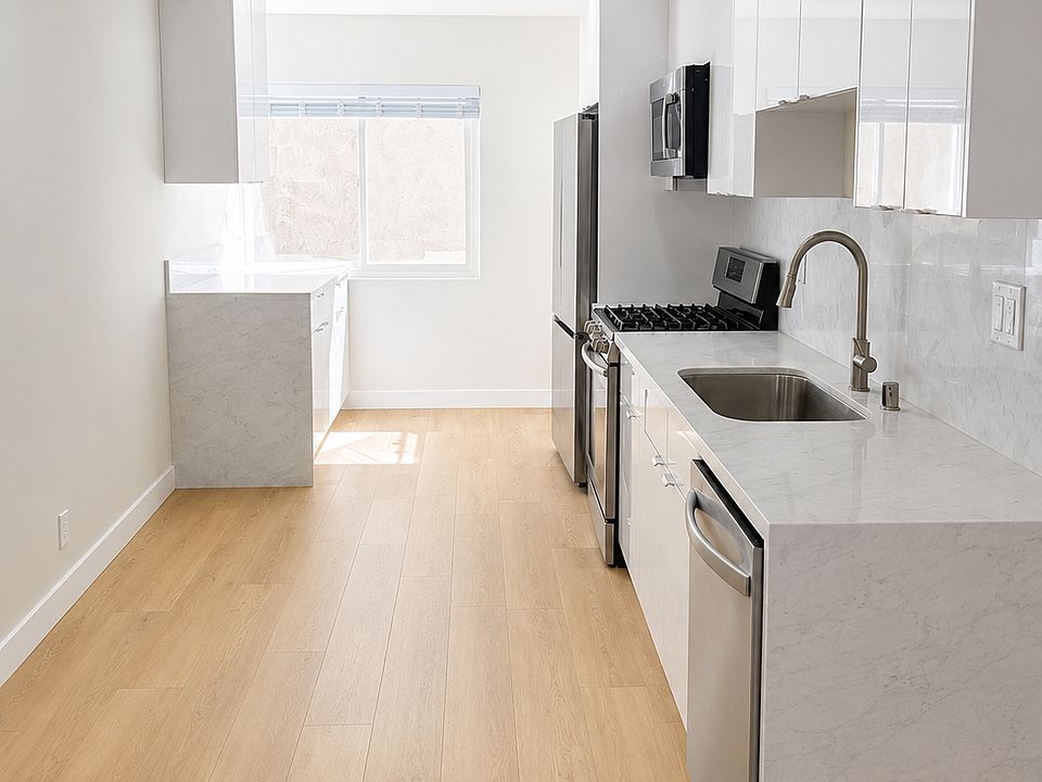 Updated kitchen with glossy white cabinetry, stainless steel appliances, marble-look counters, and full-height backsplash
