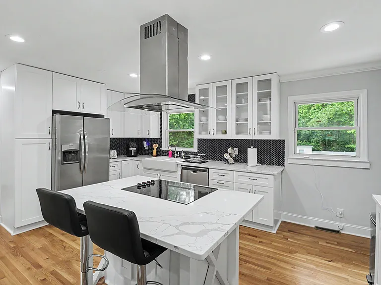 Kitchen 1: updated with white cabinetry, quartz counters, island cooktop seating, and stainless appliances.