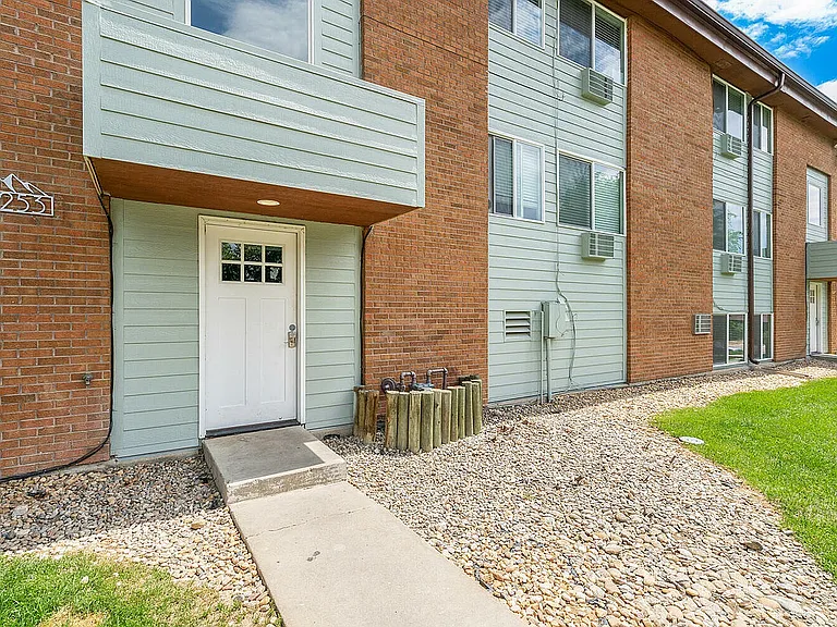 Charming brick and siding apartment exterior with modern double doors, framed by lush green lawns and decorative stone pathways.