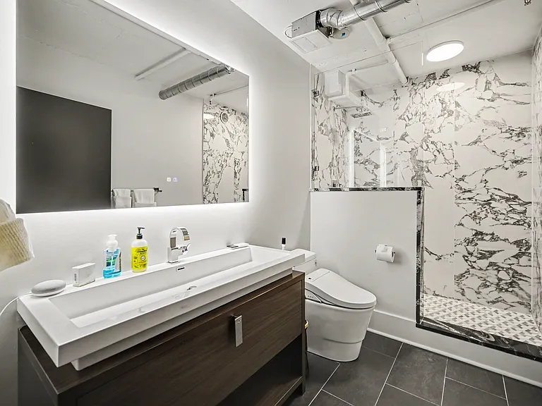 Guest bathroom next to the office features backlit mirror, wide sink, beautiful marble-like shower with rain shower head and a modern bidet
