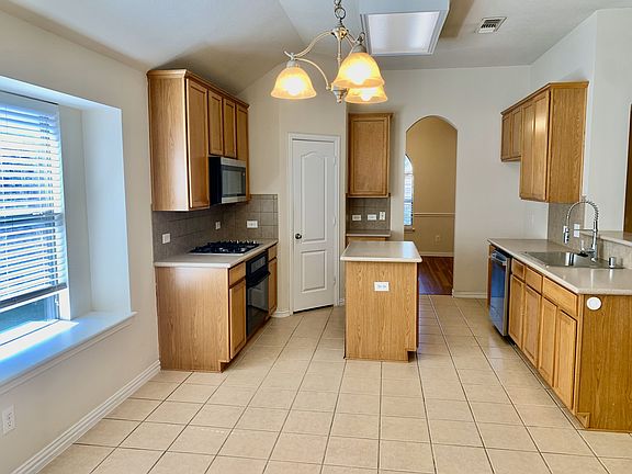 Kitchen featuring stainless steel appliances, decorative backsplash, arched walkways, light countertops, and vaulted ceiling