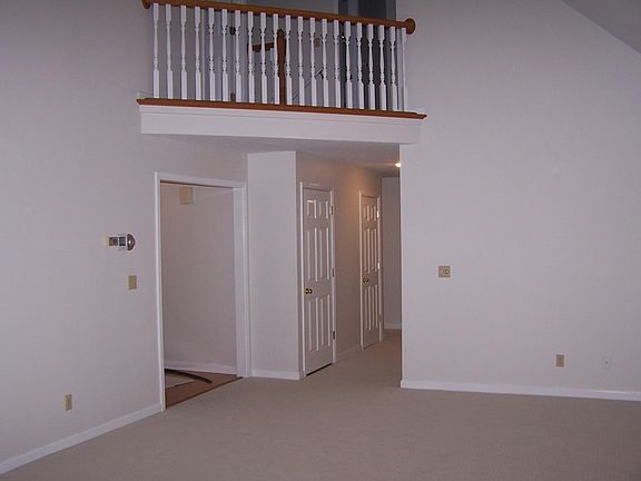 Great room showing second floor balcony, front door entry to left, and hall leading to master bedroom and 2 other bedrooms.