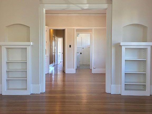 Living room with built-in bookcases; looking into the dining room, breakfast nook, kitchen and hall leading to the bedroom.