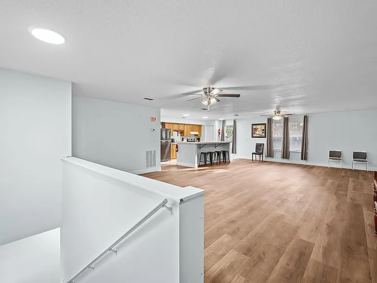 Open living area with durable wood-look flooring, ceiling fans, and a breakfast bar connecting to the kitchen.