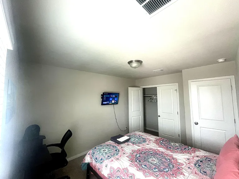 Furnished bedroom with a full bed, wall-mounted TV, desk chair, and a reach-in closet for everyday storage needs.