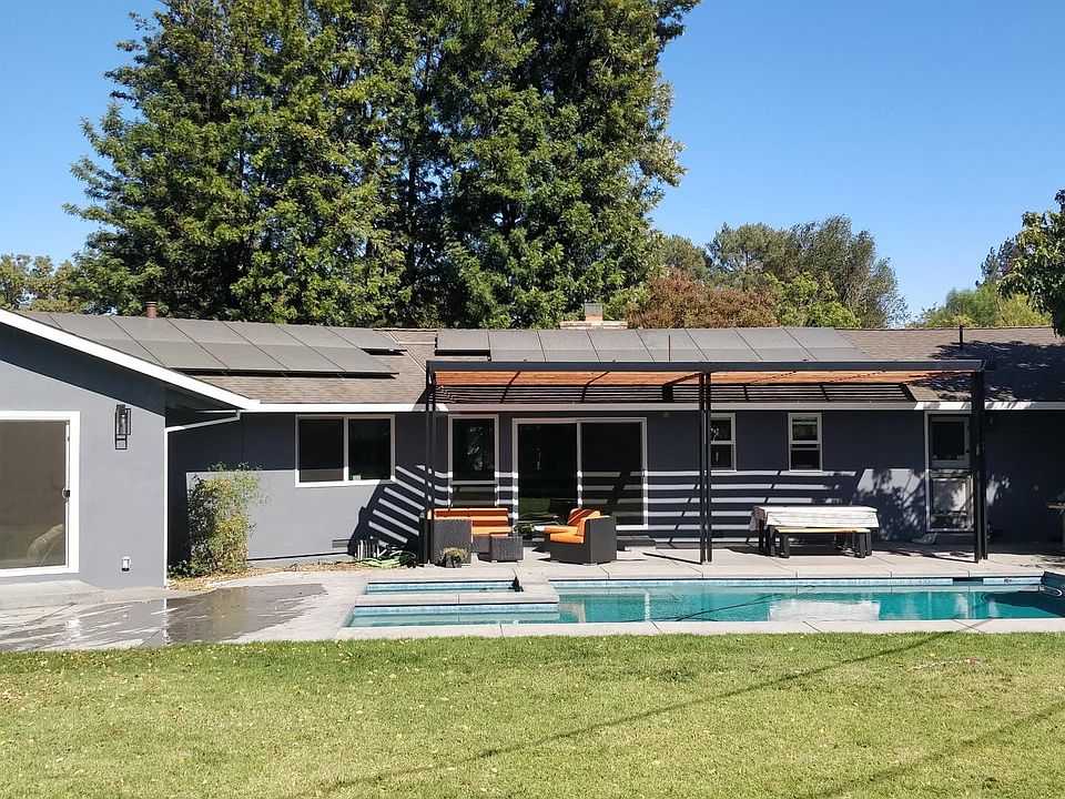 Backyard view of house with pool, jacuzzi and patio area with sofa seating and outdoor table seating.