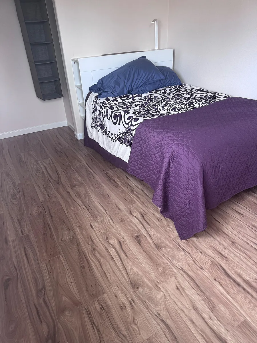 Private bedroom with wood-look flooring and a comfortable bed, featuring a headboard with built-in shelving for essentials. - Whitman Rd
