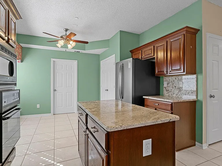 Kitchen featuring a central island with a granite countertop, built-in wall oven and microwave, dark wood cabinetry, and tile flooring