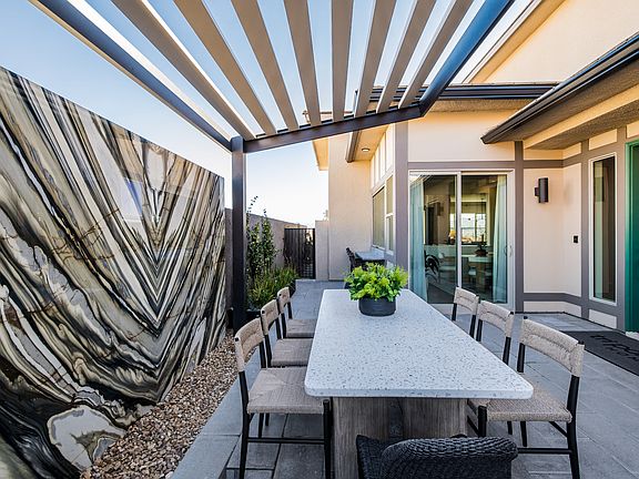 A modern outdoor patio with a wooden pergola overhead, a long concrete dining table, and chairs surr