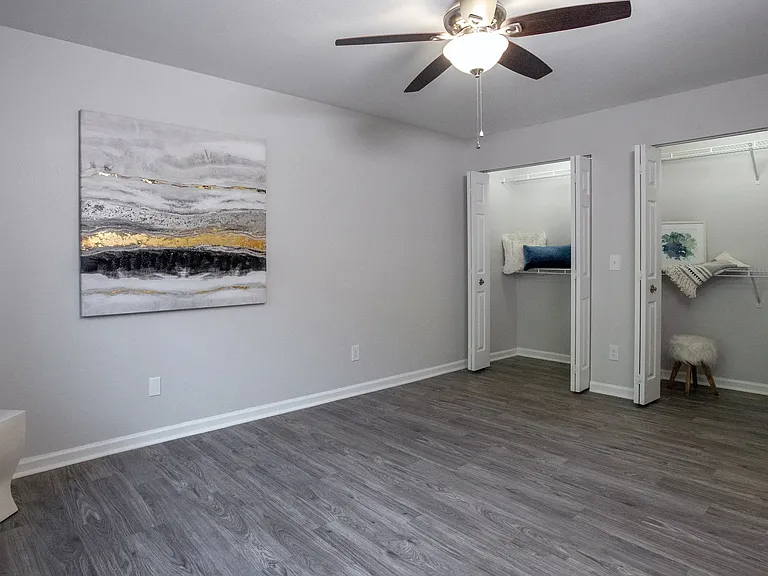 Wood-style flooring, ceiling fan, and generous closet space add a touch of elegance to this spacious bedroom.