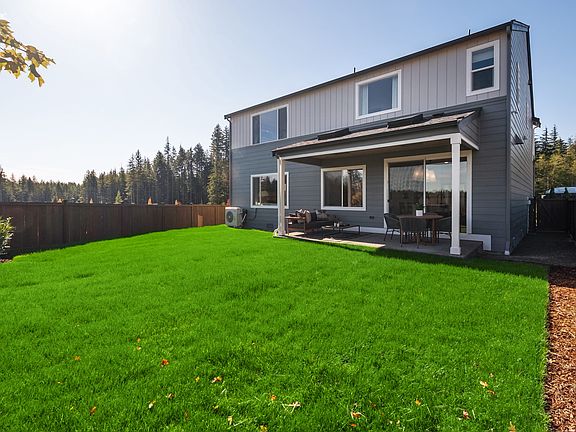 A well-maintained two-story house with a lush green lawn in the foreground, surrounded by a wooden f