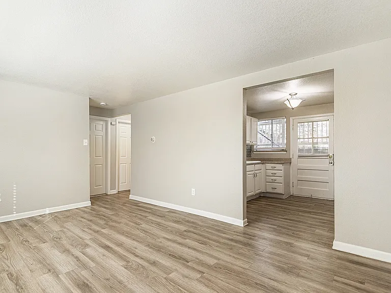 Bright and inviting living area with modern laminate flooring, leading to a cozy kitchen with natural light.