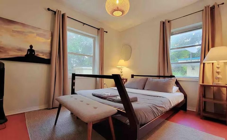 Furnished bedroom featuring a full bed, bench seating, and two windows with curtains for natural light and airflow.