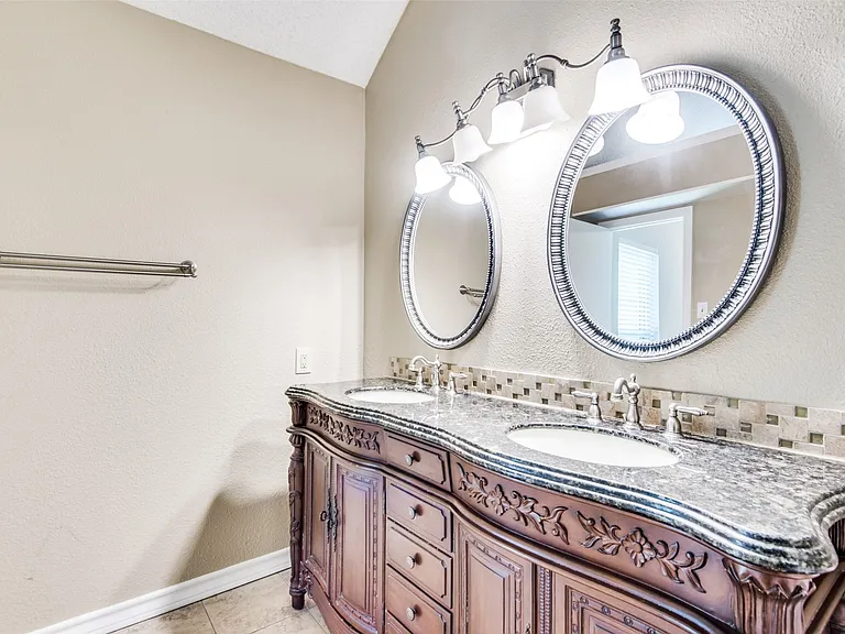 Double vanity with carved wood cabinetry, stone countertop, two oval mirrors, and brushed nickel fixtures