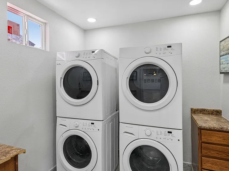 Dedicated laundry area with two stacked washer/dryer sets, overhead lighting, and a countertop for folding and storage.