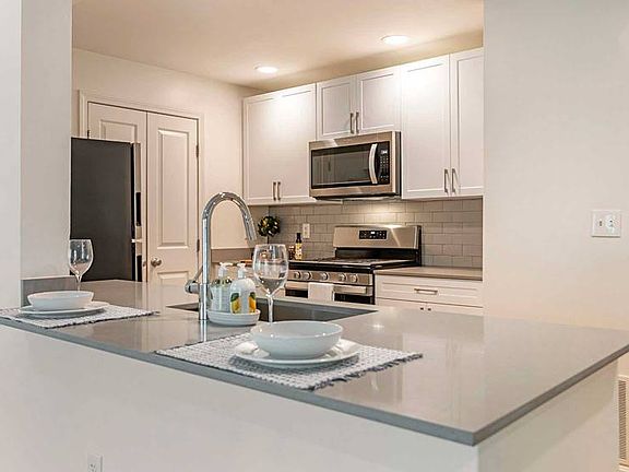 Newly renovated Finish Package II kitchen with white cabinetry, grey quartz countertops, grey tile backsplash, stainless steel appliances, and hard surface flooring