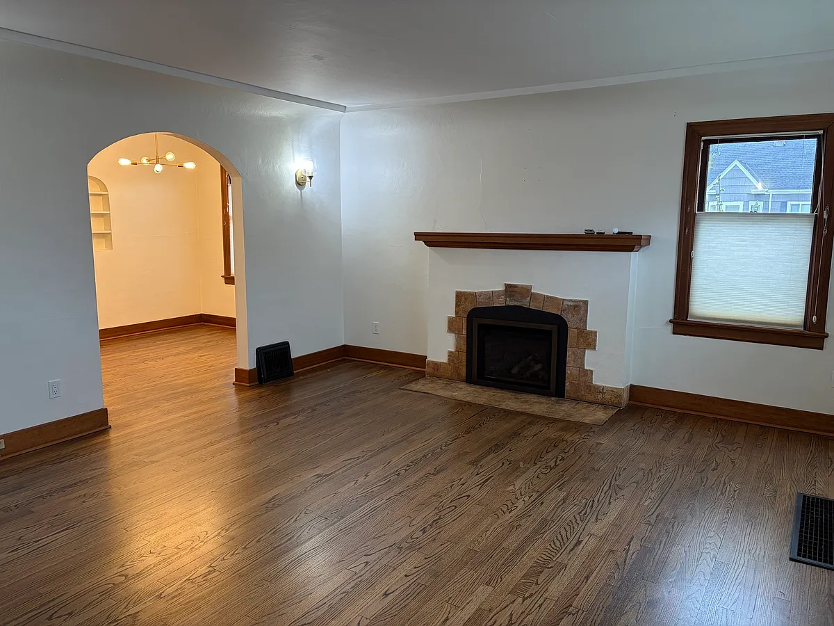 Spacious living room with original refinished hardwood floors, wood-burning fireplace with mantel, and period craftsman details throughout. Opens through an arched doorway into the dining room - 4016 N 7th St