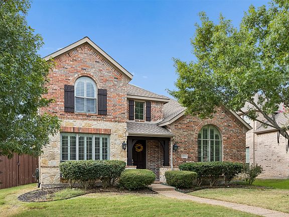 Brick and stone exterior with arched windows, dark shutters, and a covered entry