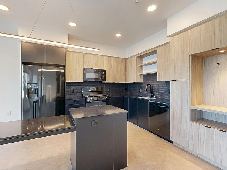 Apartment kitchen with black appliances, dark counters, and wood style floor.
