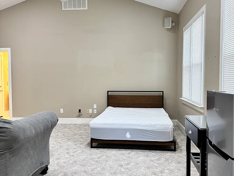 Bright 600 sq ft bedroom with a Queen-size bed and premium mattress, cozy sofa, ceiling fans, and abundant natural light.