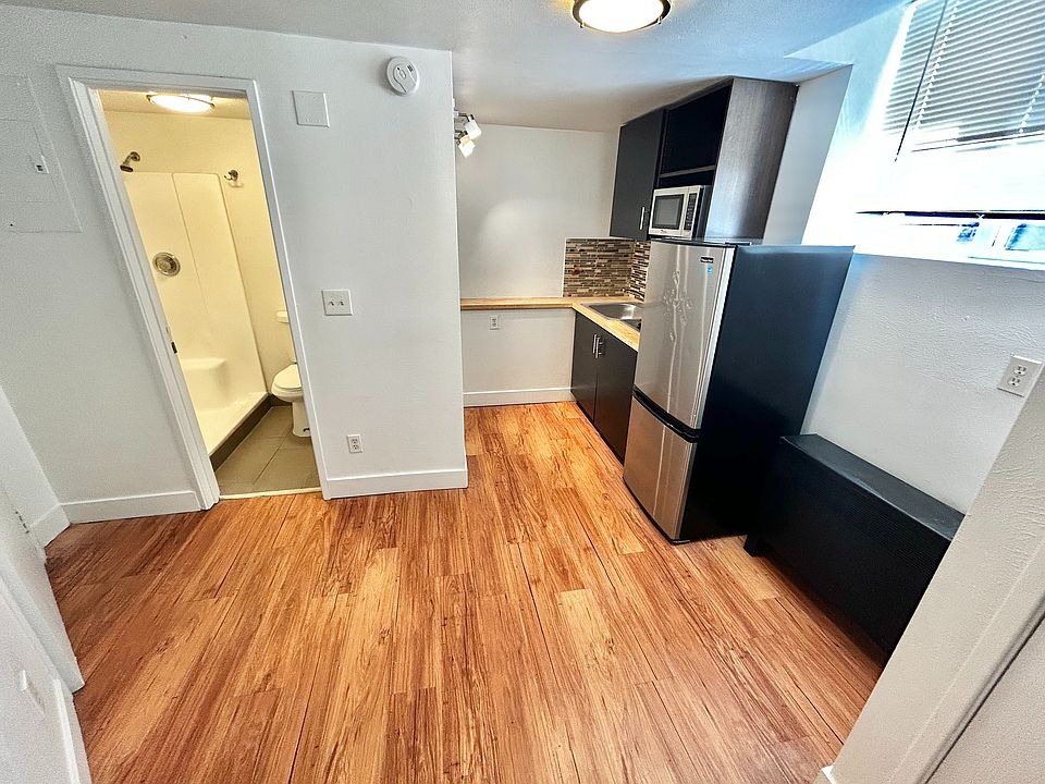 Charming apartment kitchen with sleek stainless steel appliances, warm wood flooring, and a cozy bathroom entrance.