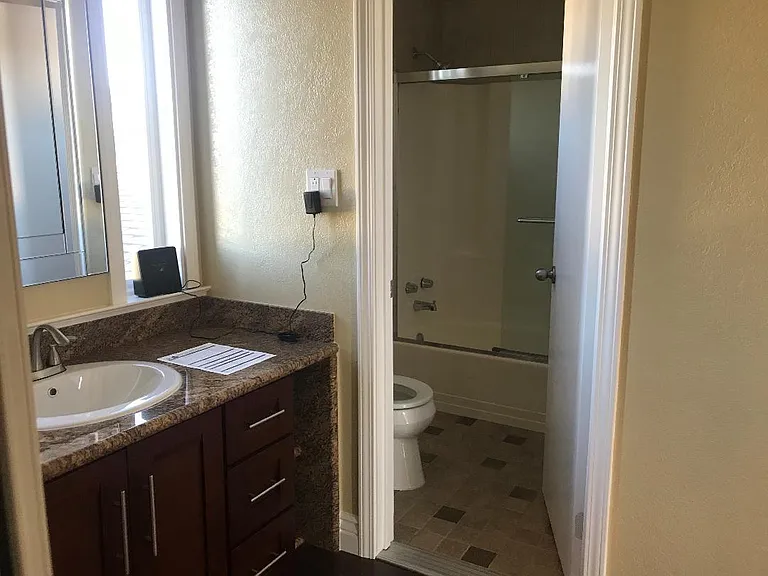 Private restroom with enclosed tub/shower combo and outside the restroom is the granate vanity and sink