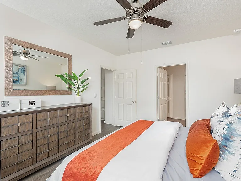 Chic bedroom with modern decor, featuring a stylish wooden dresser, vibrant pillows, and a ceiling fan, offering a cozy and inviting atmosphere.