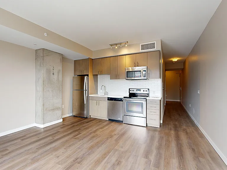 Apartment kitchen with stainless steel appliances, dining and living room with wood-style flooring.