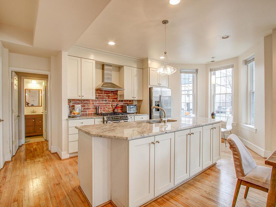 Close up of kitchen with room for a small table in front of the window, lots of cabinets, and industrial exposed brick backsplash.