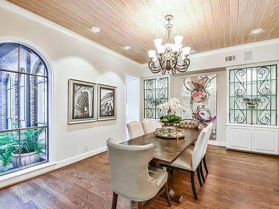 Formal dining room boasts an arched window overlooking the front courtyard entry and built ins with glass shelving and decorative iron cabinet fronts.