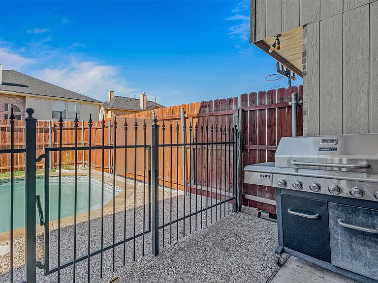 Pool area with black wrought iron fencing and a wooden privacy fence, featuring a concrete patio surface