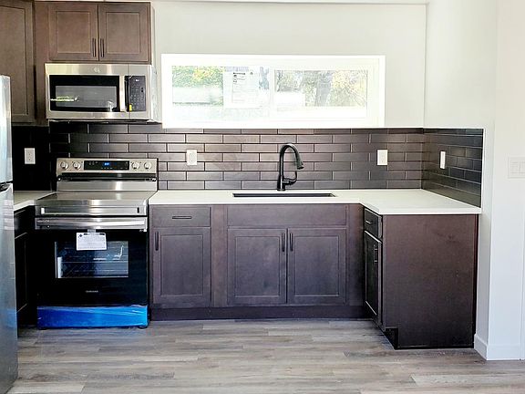 Kitchen with stainless steel refrigerator, top freezer, smart electric range, microwave, solid wood cabinets and black tile backsplash. Walk in closet to the right.