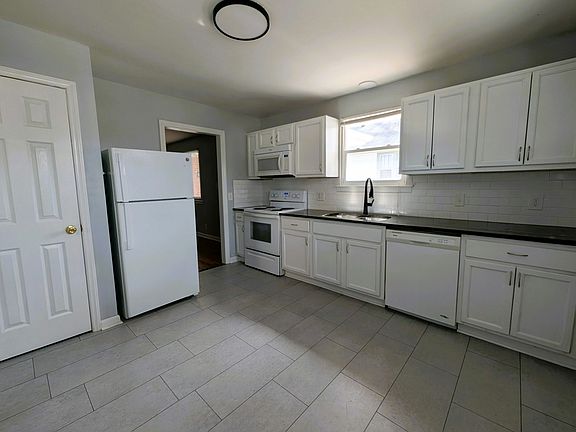 granite counters, tile flooring, subway tile backsplash and modern fixtures with a dishwasher, disposal, microwave and double sink