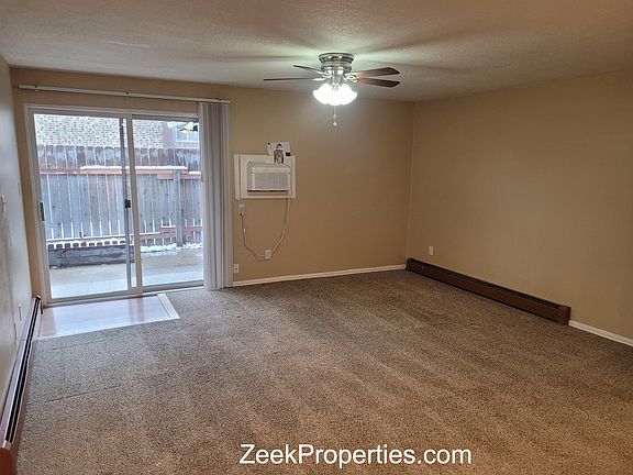 Living room with ceiling fan and Wall A/C leading to fenced yard and open area.