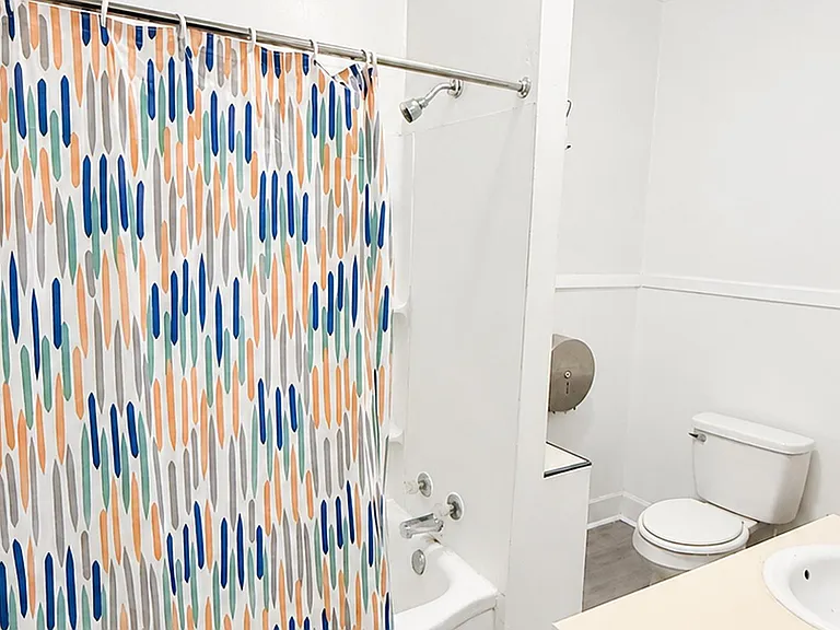 Full bathroom with a tub/shower combo, colorful shower curtain, and a vanity sink with mirror and storage.