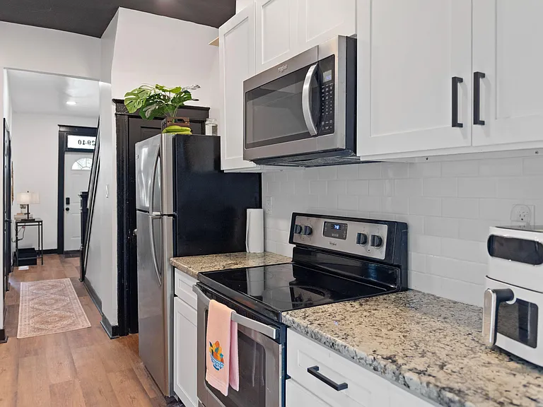Efficient galley kitchen with granite-look counters, white cabinetry, subway tile backsplash, and stainless appliances.