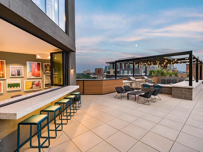Rooftop lounge with bar seating, grill stations, and shaded spaces for casual hangs or evening gatherings under the string lights.