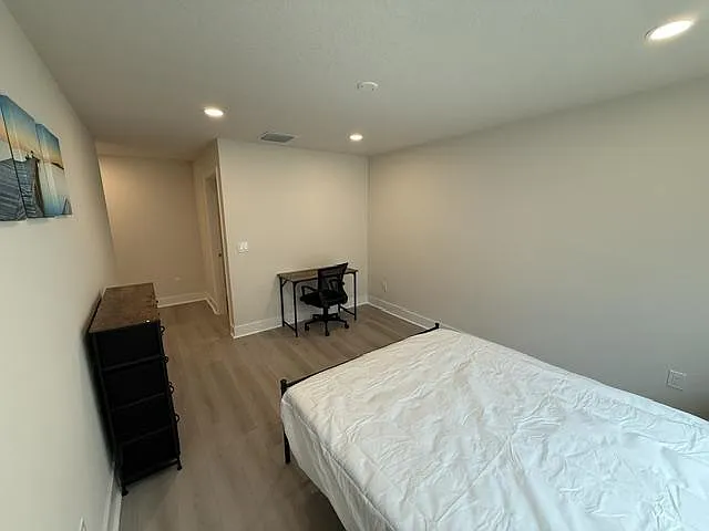 Spacious bedroom with wood-look flooring, recessed lighting, and room for a bed plus a desk setup.
